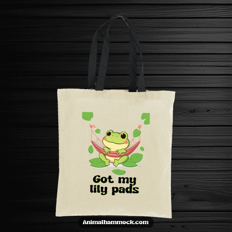 Funny green frog grinning in a hammock on a tote bag, featuring lily pads and a relaxed vibe.